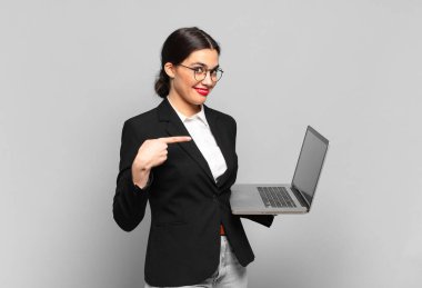 Genç, güzel bir kadın neşeyle gülümsüyor, mutlu hissediyor ve yan ve yukarı doğru işaret ediyor, fotokopi uzayında nesneler gösteriyor. dizüstü bilgisayar