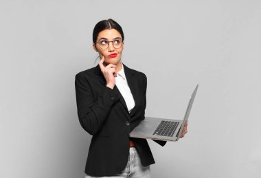 Genç, güzel bir kadın düşünüyor, kuşkulu ve şaşkın hissediyor, farklı seçeneklerle, hangi kararı vereceğini merak ediyor. dizüstü bilgisayar