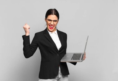 Genç ve güzel bir kadın öfkeli bir ifadeyle ya da yumruklarıyla başarıyı kutlarken agresif bir şekilde bağırıyor. dizüstü bilgisayar