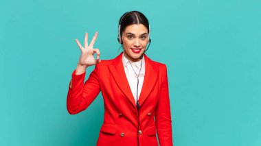 Genç, güzel bir kadın kendini mutlu, rahat ve tatmin olmuş hissediyor. İyi bir jestle onaylıyor, gülümsüyor. tele pazarlamacı kavramı