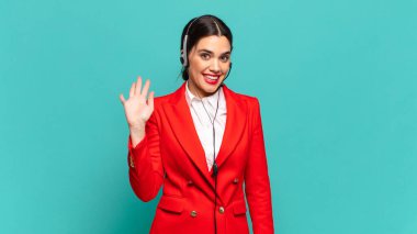 Genç ve güzel bir kadın mutlu ve neşeli bir şekilde gülümsüyor, el sallıyor, sizi selamlıyor ve selamlıyor, ya da veda ediyor. tele pazarlamacı kavramı