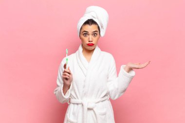 Genç ve güzel bir kadın şaşkın ve şaşkın hissediyor, şüpheci, farklı seçenekleri tartıyor ya da komik bir ifadeyle seçiyor. Bornoz ve diş fırçası kavramı