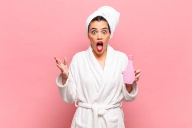 Genç ve güzel bir kadın ağzı açık ve şaşırmış, şok olmuş ve hayrete düşmüş inanılmaz bir sürprizle. Bornoz ve yüz temizleme konsepti