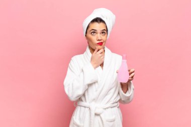 Genç, güzel bir kadın düşünüyor, kuşkulu ve şaşkın hissediyor, farklı seçeneklerle, hangi kararı vereceğini merak ediyor. Bornoz ve yüz temizleme konsepti