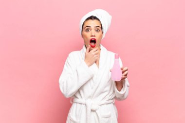 Ağzı ve gözleri açık, eli çenesinde genç ve güzel bir kadın. Hoş olmayan bir şok geçiriyor. Ne diyor? Bornoz ve yüz temizleme konsepti