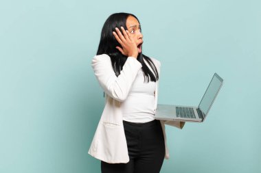 Genç siyahi kadın mutlu, heyecanlı ve şaşırmış hissediyordu. İki eli de suratında bir tarafa bakıyordu. dizüstü bilgisayar