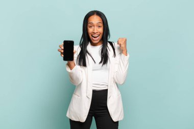 Genç siyahi kadın şok olmuş, heyecanlı ve mutlu hissediyor, gülüyor ve başarıyı kutluyor, vay canına! akıllı telefon kavramı