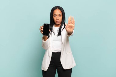 Genç siyahi kadın ciddi, sert, hoşnutsuz ve kızgın görünüyor. akıllı telefon kavramı