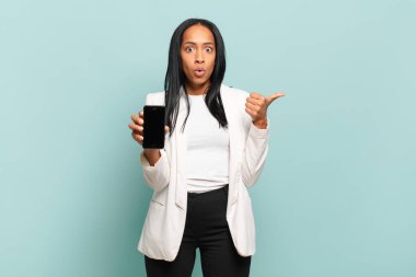 Genç siyahi kadın inançsızlıktan şaşkın şaşkın bakıyor, yan taraftaki objeyi işaret ediyor ve 