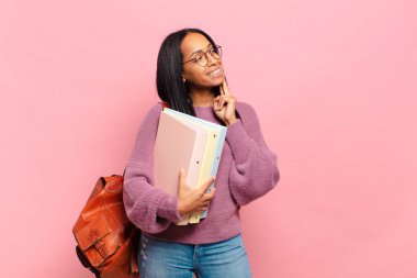 Genç siyahi kadın mutlu bir şekilde gülümsüyor ve hayal kuruyor ya da şüphe ediyor, yan tarafa bakıyor. öğrenci konsepti