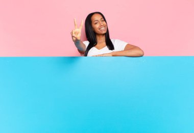 Genç siyah kadın gülümsüyor ve mutlu görünüyor, kaygısız ve olumlu, zafer ya da barışı simgeliyor. boşluk konseptini kopyala