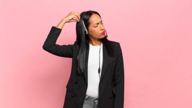 Genç siyahi kadın şaşkın ve kafası karışmış hissediyor. Kafasını kaşıyor ve yana bakıyor. tele pazarlama kavramı