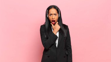 Ağzı ve gözleri açık, eli çenesinde genç siyah bir kadın. Hoş olmayan bir şok geçiriyor. Ne diyor? tele pazarlama kavramı