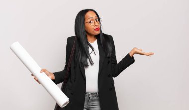 Genç siyahi kadın şaşkın ve şaşkın hissediyor, şüpheci, farklı seçenekleri tartıyor ya da komik bir ifadeyle seçiyor. mimar konsepti 