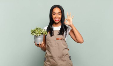 Genç siyahi kadın mutlu, rahat ve tatmin olmuş hissediyor. Onayını iyi bir hareketle gösteriyor. Gülümsüyor. Bahçıvan konsepti