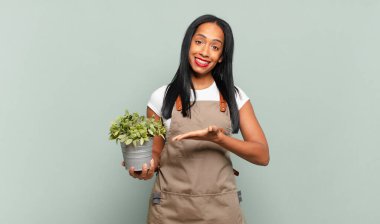 Genç siyahi kadın neşeyle gülümsüyor, mutlu hissediyor ve fotokopi uzayı içinde avucunun içi gibi bir konsept gösteriyor. Bahçıvan konsepti
