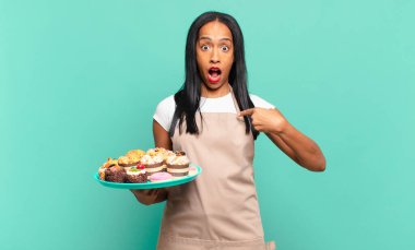 Genç siyahi kadın şok olmuş ve ağzı açık, kendini işaret ederek şaşırmış görünüyor. Fırın şefi konsepti