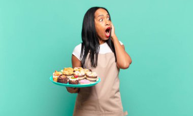 Genç siyahi kadın mutlu, heyecanlı ve şaşırmış hissediyordu. İki eli de suratında bir tarafa bakıyordu. Fırın şefi konsepti