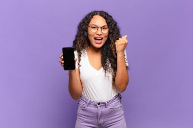 Genç İspanyol kadın şok olmuş, heyecanlı ve mutlu hissediyor, gülüyor ve başarıyı kutluyor, vay canına! akıllı telefon kavramı