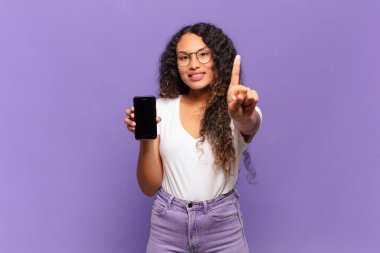 Genç İspanyol kadın gururla gülümsüyor ve gururla bir numaralı pozunu veriyor, kendini lider gibi hissediyor. akıllı telefon kavramı