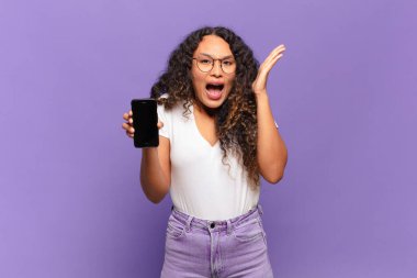 Genç İspanyol kadın mutlu, heyecanlı, şaşırmış ya da şok olmuş hissediyor. İnanılmaz bir şeye gülümsüyor ve hayrete düşüyor. akıllı telefon kavramı