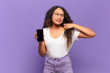 Genç İspanyol kadın stresli, endişeli, yorgun ve hayal kırıklığına uğramış, gömleğini çekmiş, sorunlu görünüyor. akıllı telefon kavramı