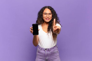 Genç İspanyol kadın gülümsüyor ve arkadaş canlısı görünüyor, bir numara ya da ilk eli önde, geriye doğru sayıyor. akıllı telefon kavramı