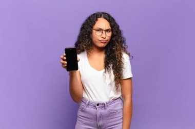 Genç İspanyol kadın üzgün, üzgün ya da kızgın hissediyor ve olumsuz bir tavırla taraflara bakıyor, anlaşmazlık içinde kaşlarını çatıyor. akıllı telefon kavramı