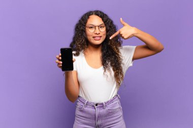 Genç İspanyol kadın kendine güvenerek gülümsüyor. Geniş gülümseme, pozitif, rahat, tatmin olmuş tavır. akıllı telefon kavramı