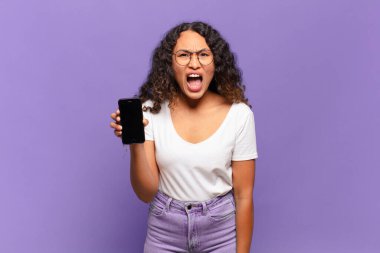 Genç İspanyol kadın agresif bir şekilde bağırıyor, çok kızgın, hayal kırıklığına uğramış, öfkeli ya da sinirli görünüyor, hayır diye bağırıyor. akıllı telefon kavramı