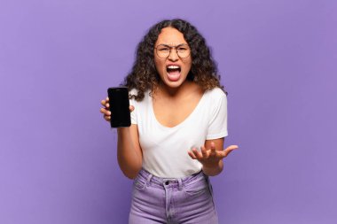 Genç İspanyol bir kadın kızgın, sinirli ve sinirli görünüyor. Senin neyin var, neyin yok? akıllı telefon kavramı 