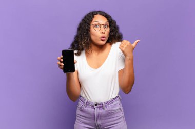 Genç İspanyol kadın inançsızlıktan şaşkın şaşkın bakıyor, yan taraftaki objeyi işaret edip 