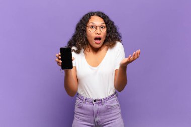 Genç İspanyol kadın ağzı açık ve şaşırmış, şok olmuş ve inanılmaz bir sürprizle şaşkına dönmüş. akıllı telefon kavramı