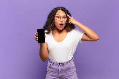 Genç İspanyol kadın şaşırmış, ağzı açık, şok olmuş, yeni bir düşünce, fikir ya da konsept keşfediyor. akıllı telefon kavramı