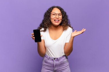 Genç İspanyol kadın mutlu, şaşırmış ve neşeli hissediyor, olumlu bir tavırla gülümsüyor, bir çözüm ya da fikrin farkına varıyor. akıllı telefon kavramı