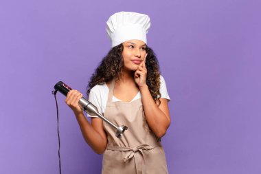 Genç İspanyol kadın mutlu bir şekilde gülümsüyor ve hayal kuruyor ya da şüphe ediyor, yana bakıyor. Şef konsepti