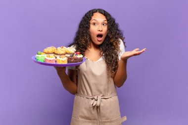 Genç İspanyol kadın ağzı açık ve şaşırmış, şok olmuş ve inanılmaz bir sürprizle şaşkına dönmüş. kek pişirme kavramı