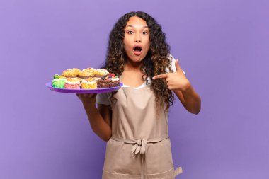 Genç İspanyol kadın şok olmuş ve ağzı açık, kendini işaret ederek şaşırmış görünüyor. kek pişirme kavramı