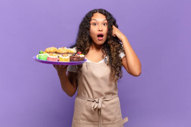 Genç İspanyol kadın şaşırmış, ağzı açık, şok olmuş, yeni bir düşünce, fikir ya da konsept keşfediyor. kek pişirme kavramı