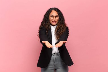 Genç İspanyol kadın mutlu bir şekilde gülümsüyor arkadaş canlısı, kendinden emin, olumlu bakışlı, bir nesne ya da konsept sunuyor ve gösteriyor. iş kavramı