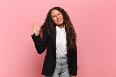 Genç İspanyol kadın mutlu ve neşeli bir şekilde gülümsüyor, el sallıyor, sizi selamlıyor ve selamlıyor, ya da veda ediyor. iş kavramı