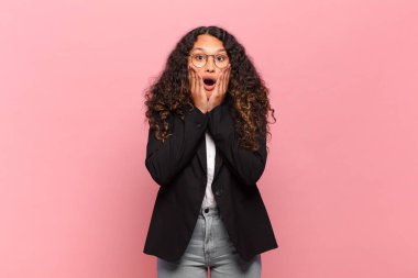 Genç İspanyol kadın şok olmuş ve korkmuş hissediyor, ağzı açık ve elleri yanaklarında korkmuş görünüyor. iş kavramı