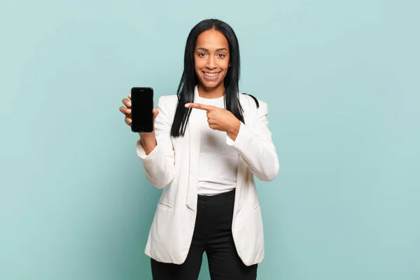 年轻的黑人妇女兴高采烈地微笑着 感到快乐 指指点着旁边和上面 在复制的空间里展示着物体 智能手机的概念 — 图库照片