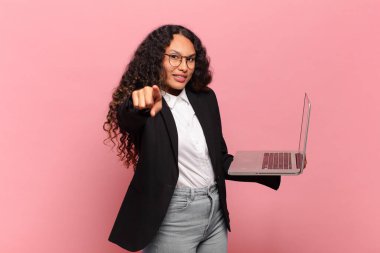 Genç İspanyol kadın kameraya tatmin olmuş, kendine güvenen, dost canlısı bir gülümsemeyle bakıyor ve seni seçiyor. dizüstü bilgisayar