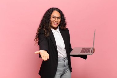 Genç İspanyol kadın mutlu bir şekilde gülümsüyor arkadaş canlısı, kendinden emin, olumlu bakışlı, bir nesne ya da konsept sunuyor ve gösteriyor. dizüstü bilgisayar