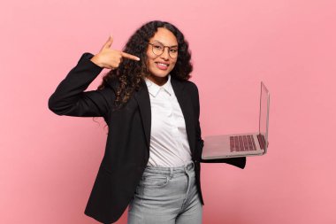 Genç İspanyol kadın kendine güvenerek gülümsüyor. Geniş gülümseme, pozitif, rahat, tatmin olmuş tavır. dizüstü bilgisayar