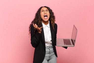 Genç İspanyol kadın umutsuz ve sinirli görünüyor, stresli, mutsuz ve sinirli, bağırıyor ve çığlık atıyor. dizüstü bilgisayar