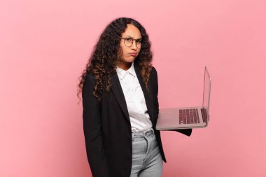 young hispanic woman feeling puzzled and confused, with a dumb, stunned expression looking at something unexpected. laptop concept
