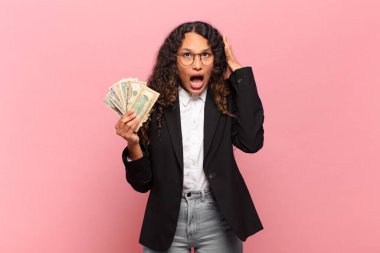 Genç İspanyol kadın elleri havada bağırıyor, öfkeli, sinirli, stresli ve üzgün hissediyor. Dolar banknotları konsepti