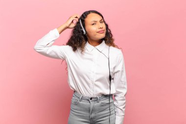 Genç İspanyol kadın şaşkın ve şaşkın hissediyor, başını kaşıyor ve yana bakıyor. tele pazarlamacı kavramı